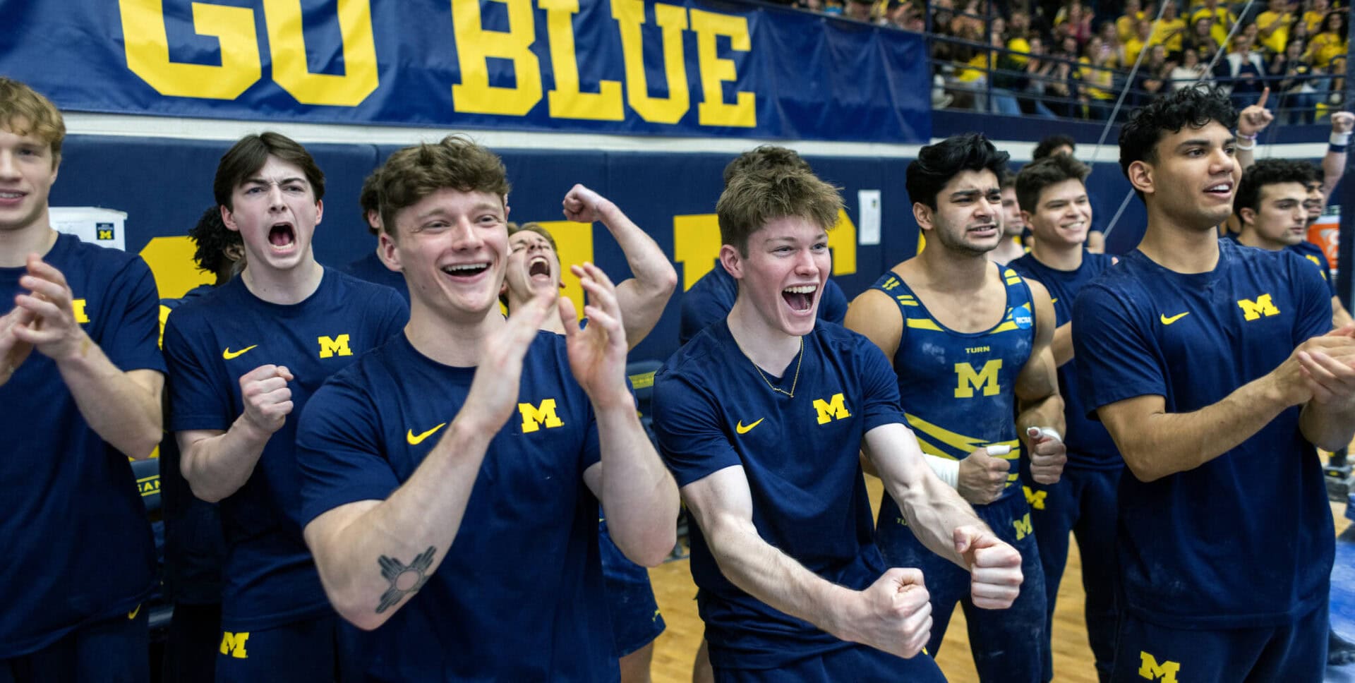 Gymnasts of the University of Michigan Men’s gymnastics team cheer as they watch their teammate perform.